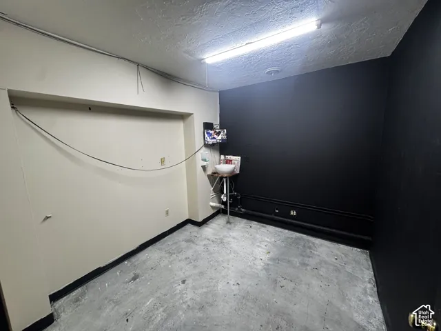 Concrete flooring with varied tones, white painted walls, black accent wall, and exposed overhead fluorescent lighting