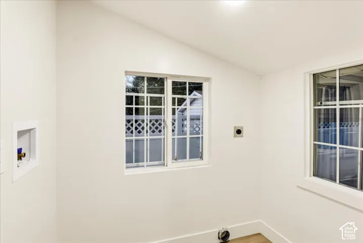 White walls with baseboard trim, two windows, and laundry hookups