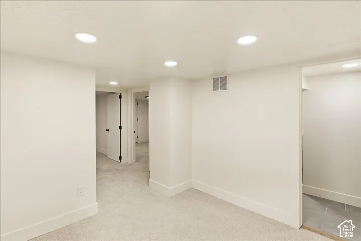 Recessed ceiling lighting, light-toned carpeting, white walls, white trim, and a doorway with a dark knob