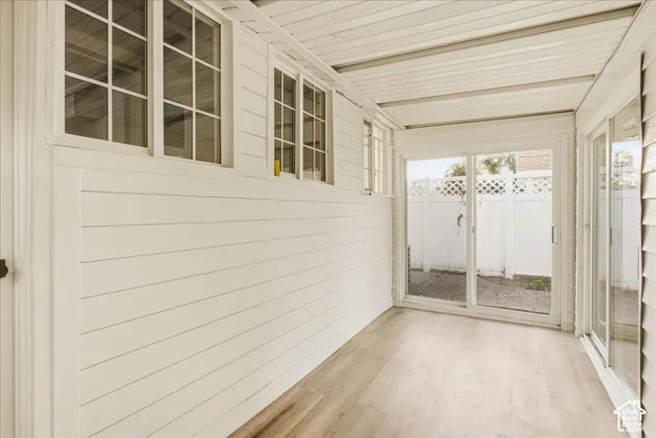 Sunroom featuring wood-finish flooring, white shiplap walls, multiple windows, and a sliding glass door