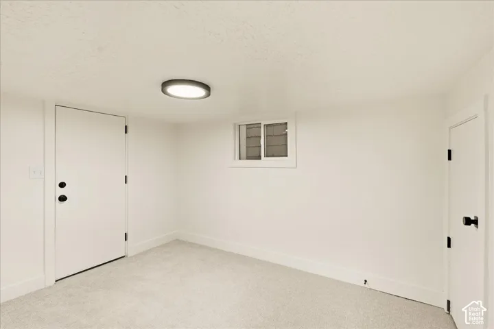 Light grey carpet flooring, white walls, flush mount ceiling light fixture, white interior doors with matte black hardware, and a single pane window