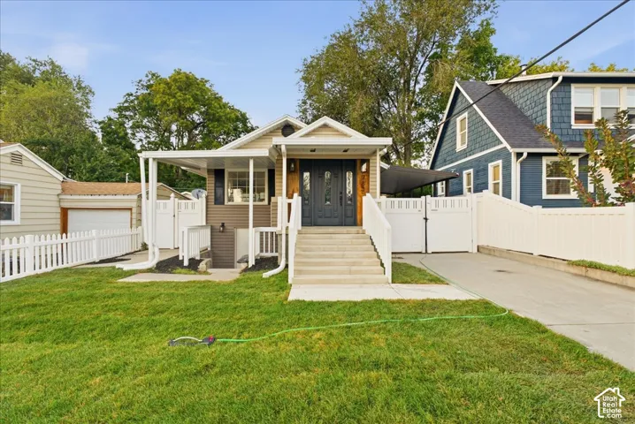 Front exterior featuring a covered porch, established lawn, concrete driveway, and white picket fencing