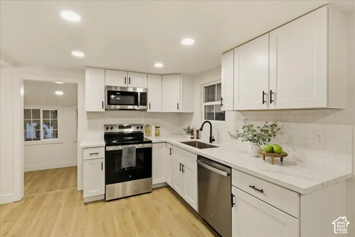 Contemporary kitchen featuring white cabinetry, light-toned wood-finish flooring, a stainless steel appliance suite, white countertops, and a white subway tile backsplash
