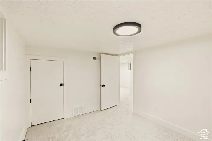 Recessed ceiling light fixture, white walls, textured ceiling, carpeted flooring, and white trim