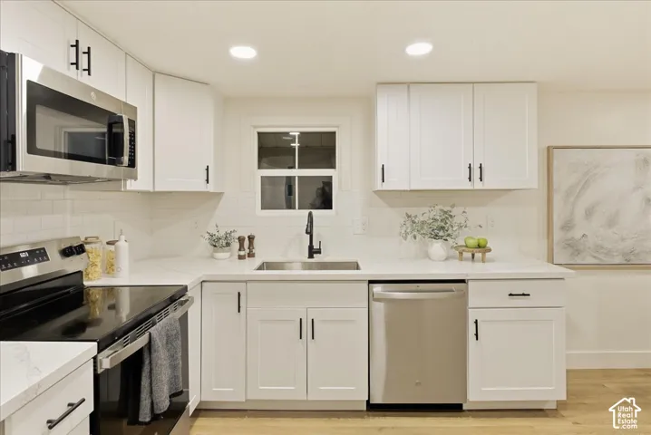 White shaker cabinetry, stainless steel appliances, undermount sink with a matte black faucet, light-colored countertops, and wood-finish flooring