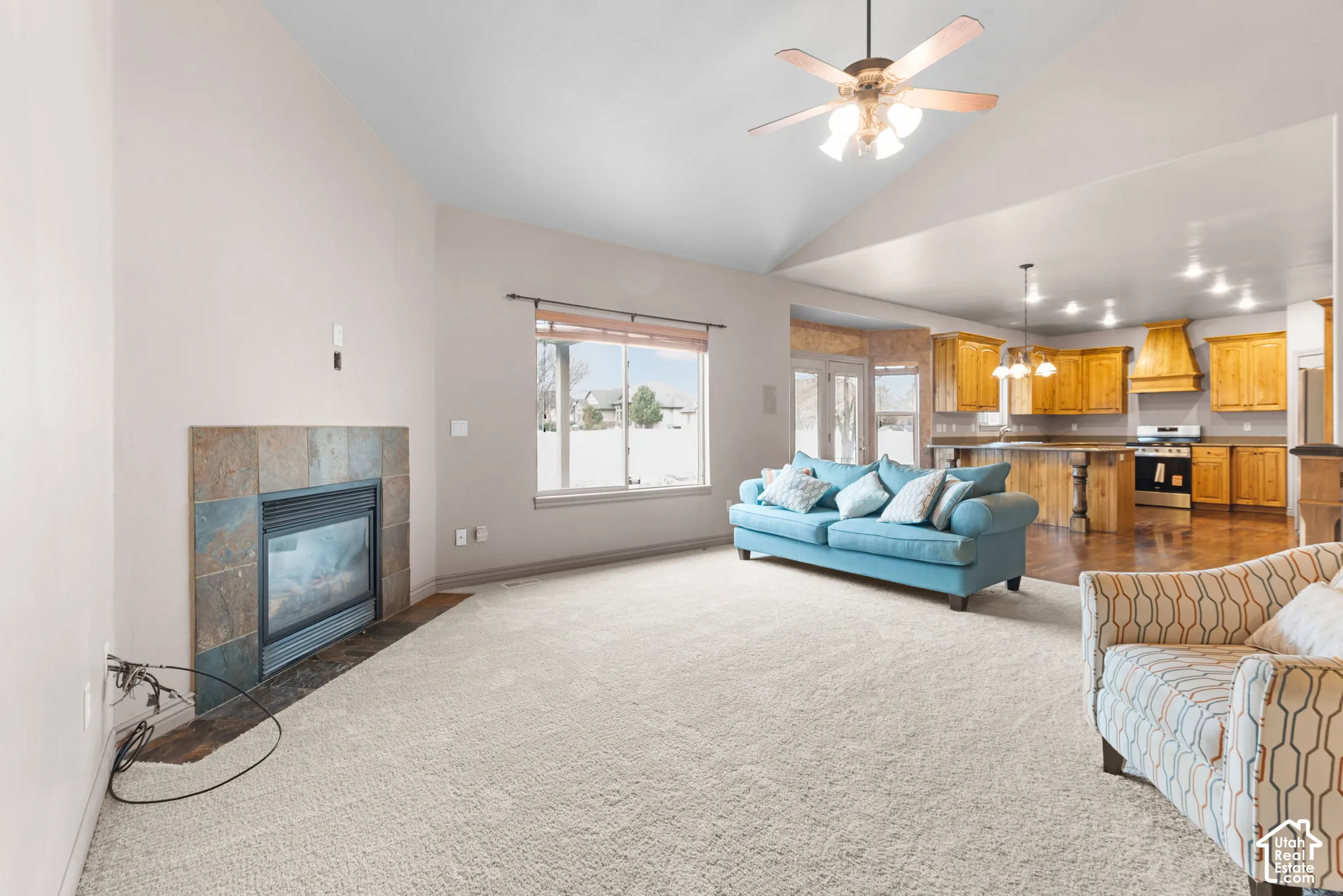 Vaulted ceiling with a ceiling fan, gas fireplace with a tile surround, large window, and wood-finish flooring in the kitchen