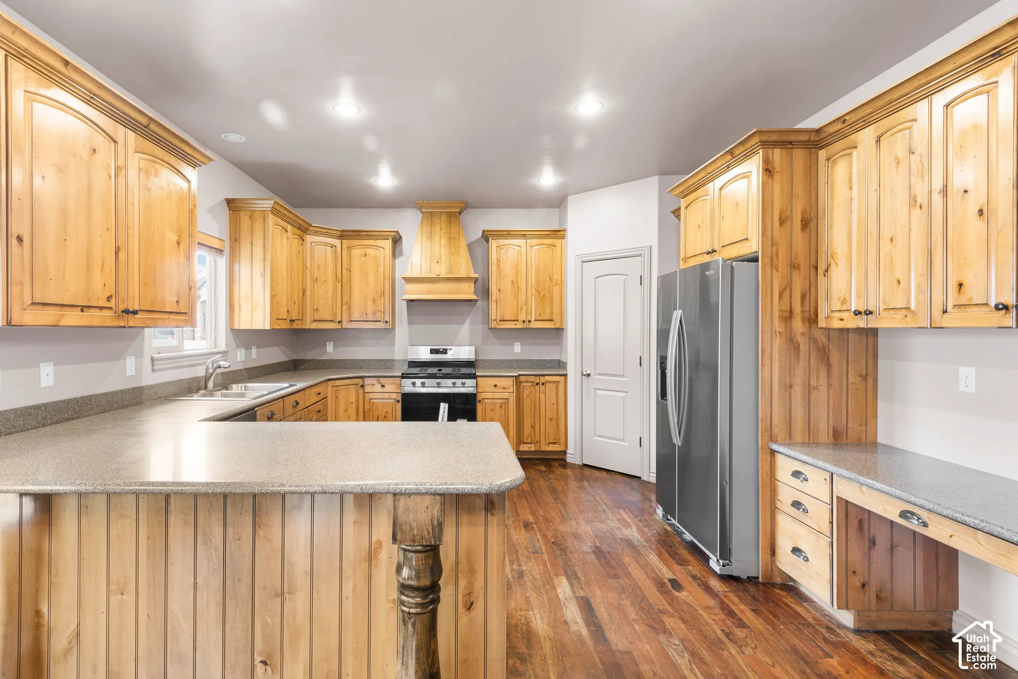Spacious kitchen featuring extensive wood cabinetry, stone-finish countertops, stainless steel appliances, and wood-finish flooring