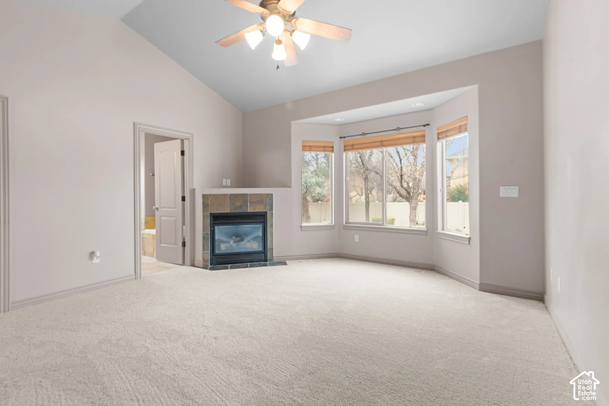 Vaulted ceiling with a ceiling fan, bay windows with blinds, tiled fireplace, and neutral carpeting