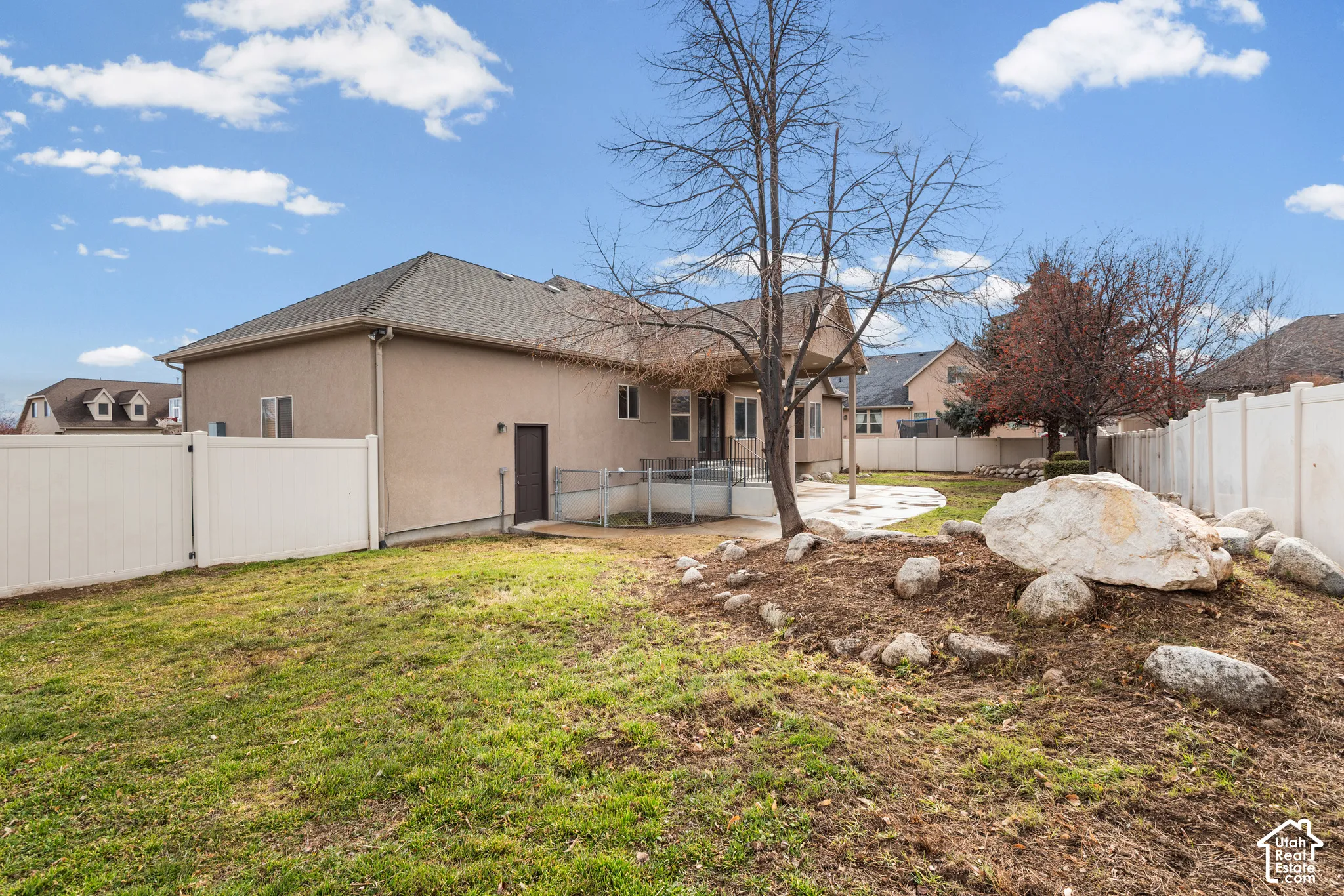 Expansive backyard featuring a stucco exterior, gravel landscaping, a white vinyl fence, and a concrete patio