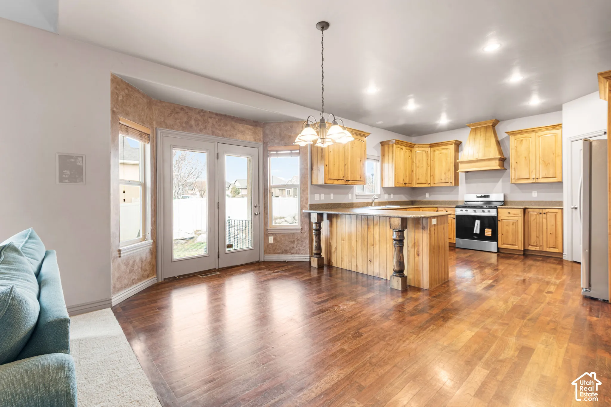Hardwood flooring, kitchen island with decorative corbels, wood cabinetry, stainless steel range, and double glass doors