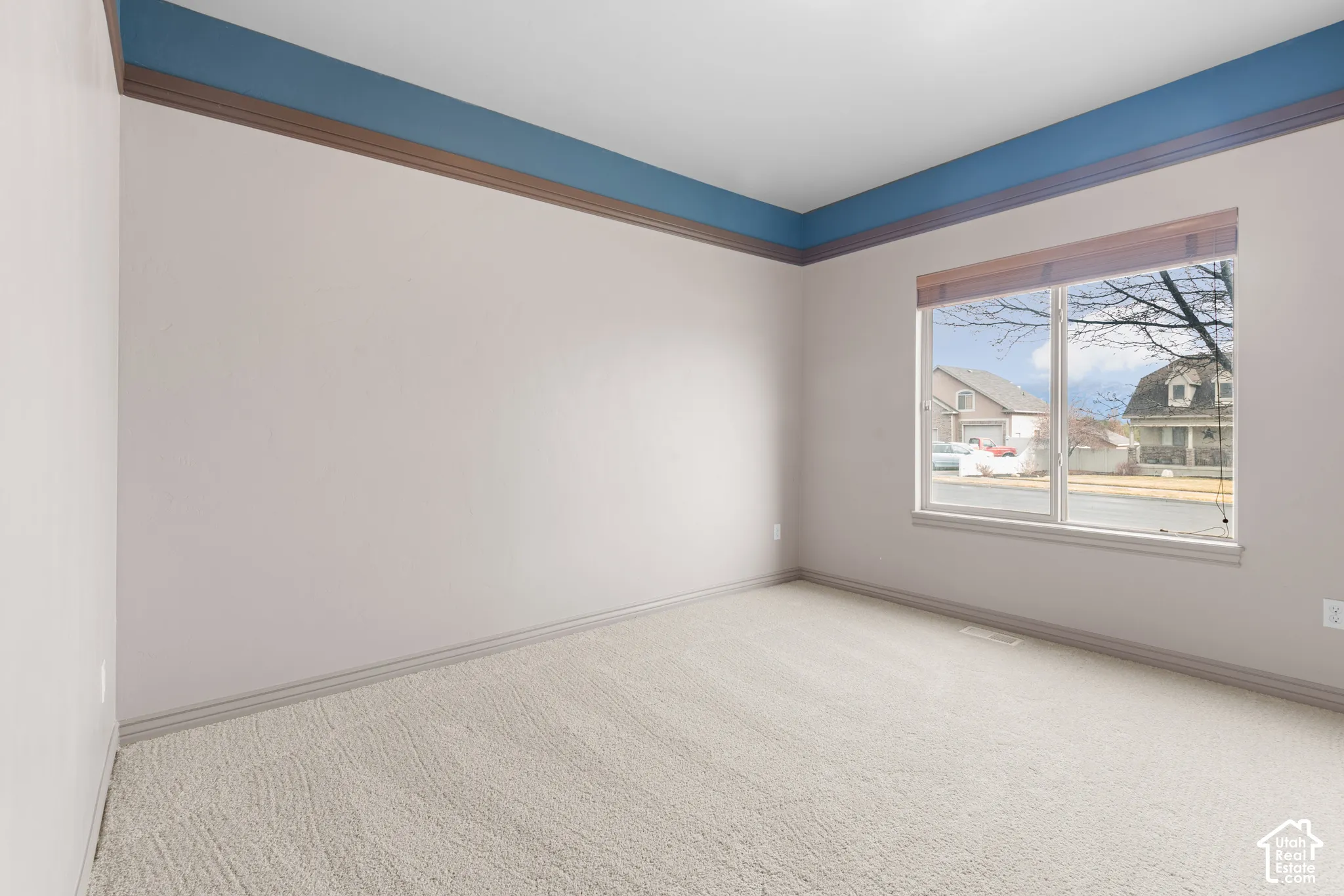 Neutral wall paint, light-toned carpet, crown molding, and a large window with blinds