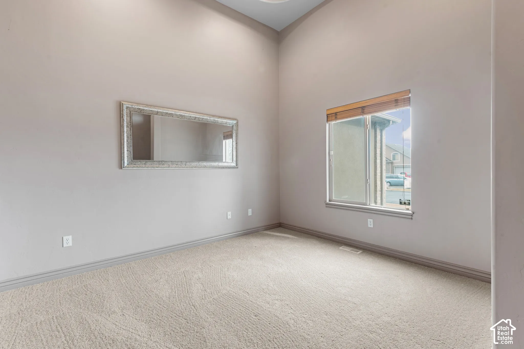 Vaulted ceiling, neutral wall paint, carpeted flooring, and window with wood-finish blinds