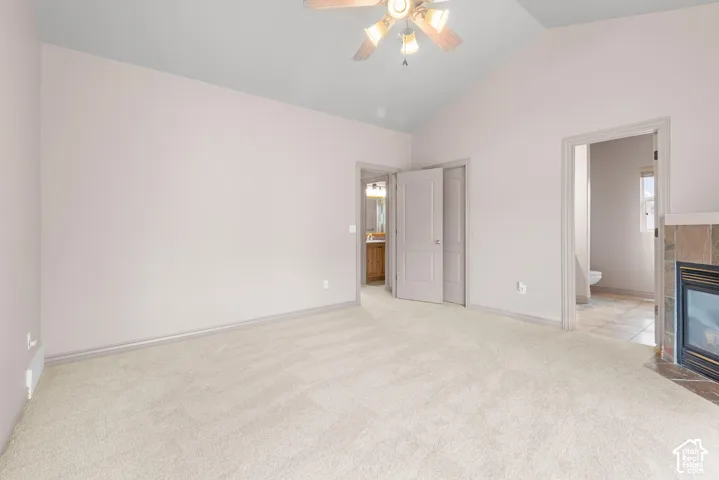 Vaulted ceiling with a ceiling fan, light-colored carpeting, and a fireplace with a tiled surround