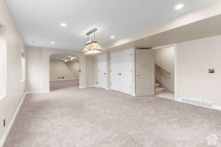 Recessed lighting, arched doorway, neutral carpeting, built-in storage closets, and interior stairway access