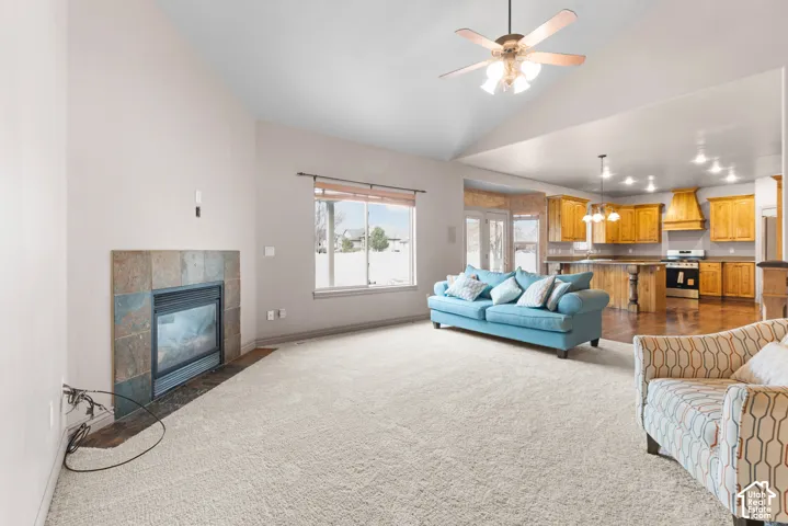 Vaulted ceiling with a ceiling fan, gas fireplace with a tile surround, large window, and wood-finish flooring in the kitchen