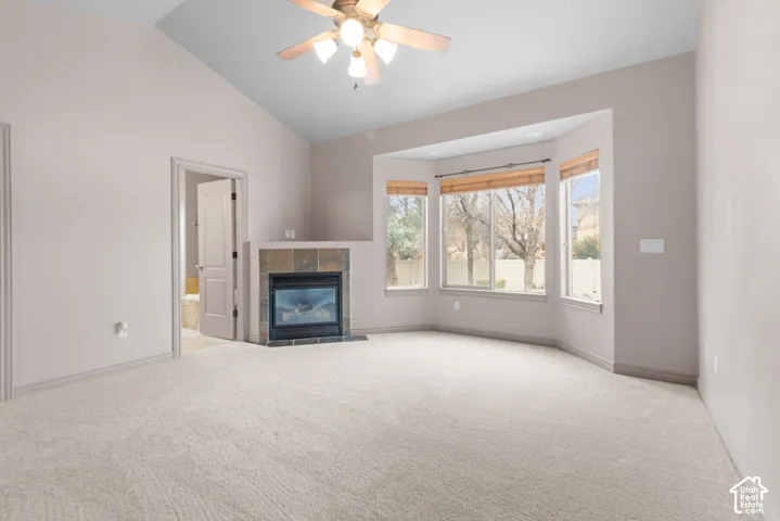Vaulted ceiling with a ceiling fan, bay windows with blinds, tiled fireplace, and neutral carpeting