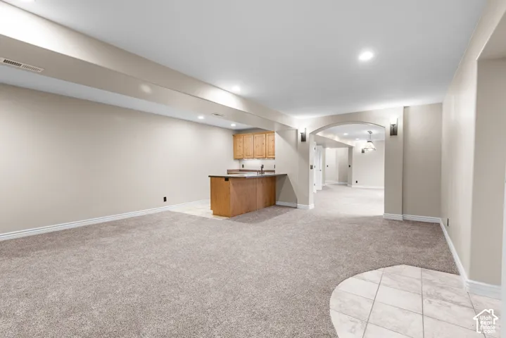 Recessed lighting, wood-finish cabinetry, countertop bar, arched doorway, and sconce lighting