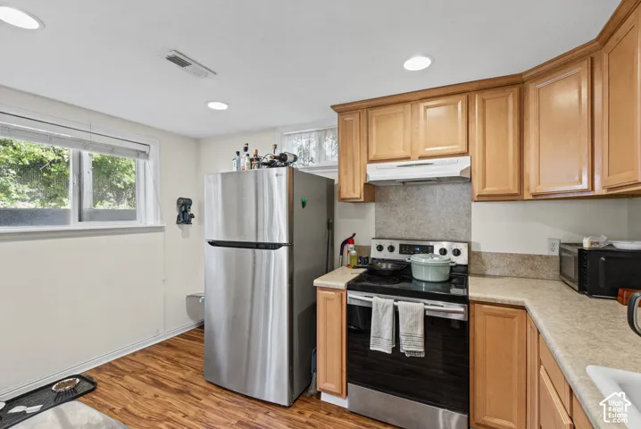 Wood-finish flooring, recessed lighting, double-hung window, light wood cabinetry, and stainless steel refrigerator