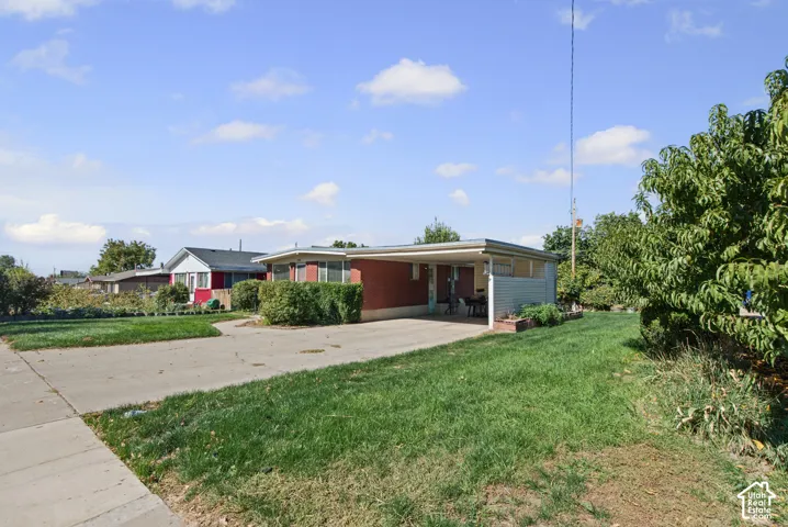 Brick exterior with carport, concrete driveway, and mature landscaping