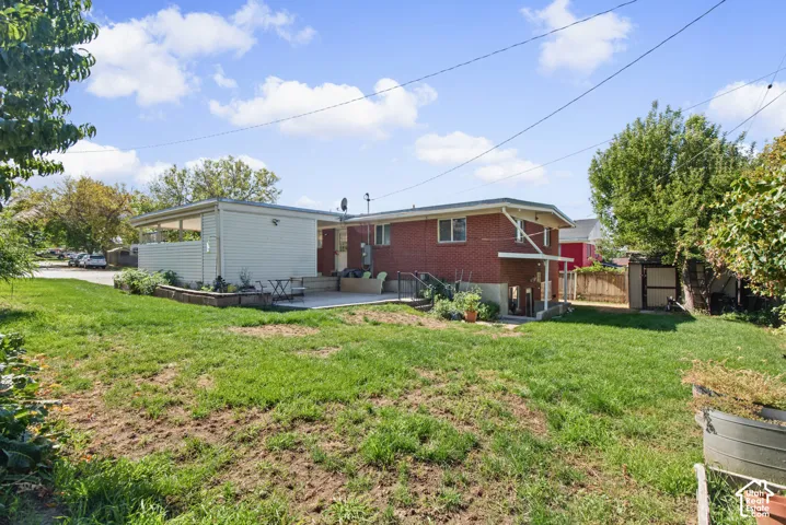 Expansive lawn featuring a concrete patio, covered patio, raised garden beds, and a brick exterior