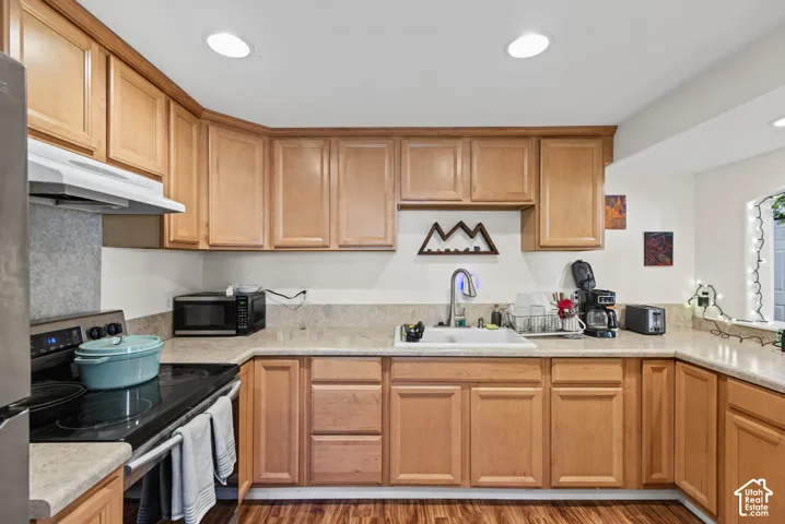 Wood-finish flooring, recessed lighting, wood cabinetry, built-in cooktop, and an integrated kitchen sink