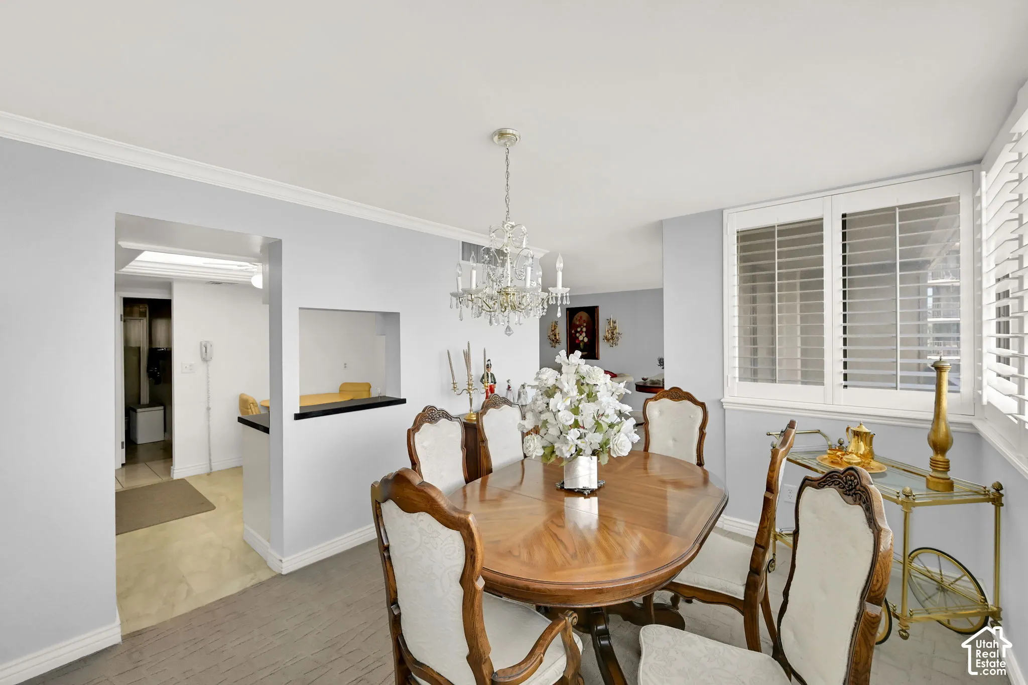 Recessed lighting, crown molding, chandelier, white plantation shutters, and a pass-through window