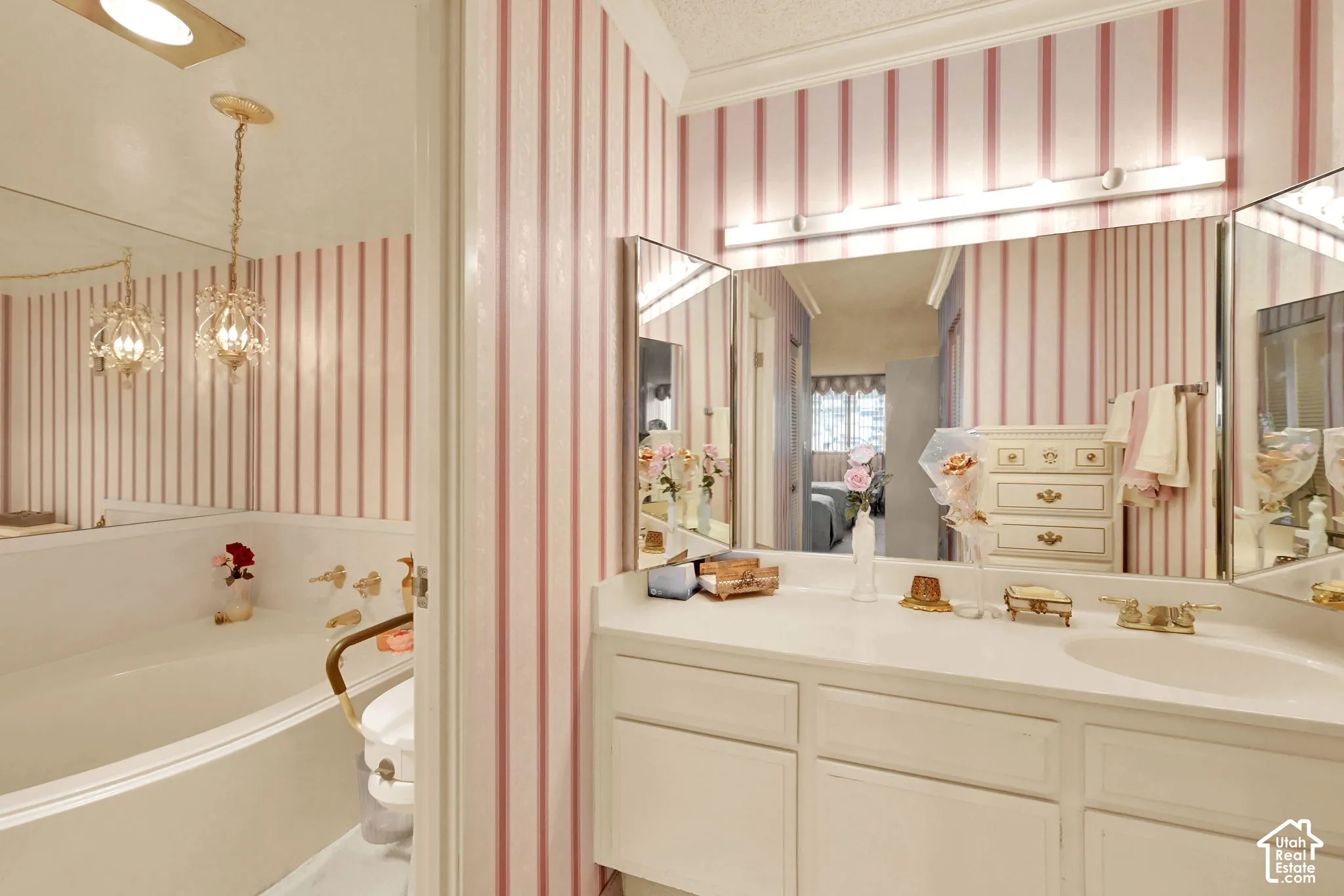 Built-in soaking tub, vanity with dual sinks, three-panel mirror, and wallpapered walls
