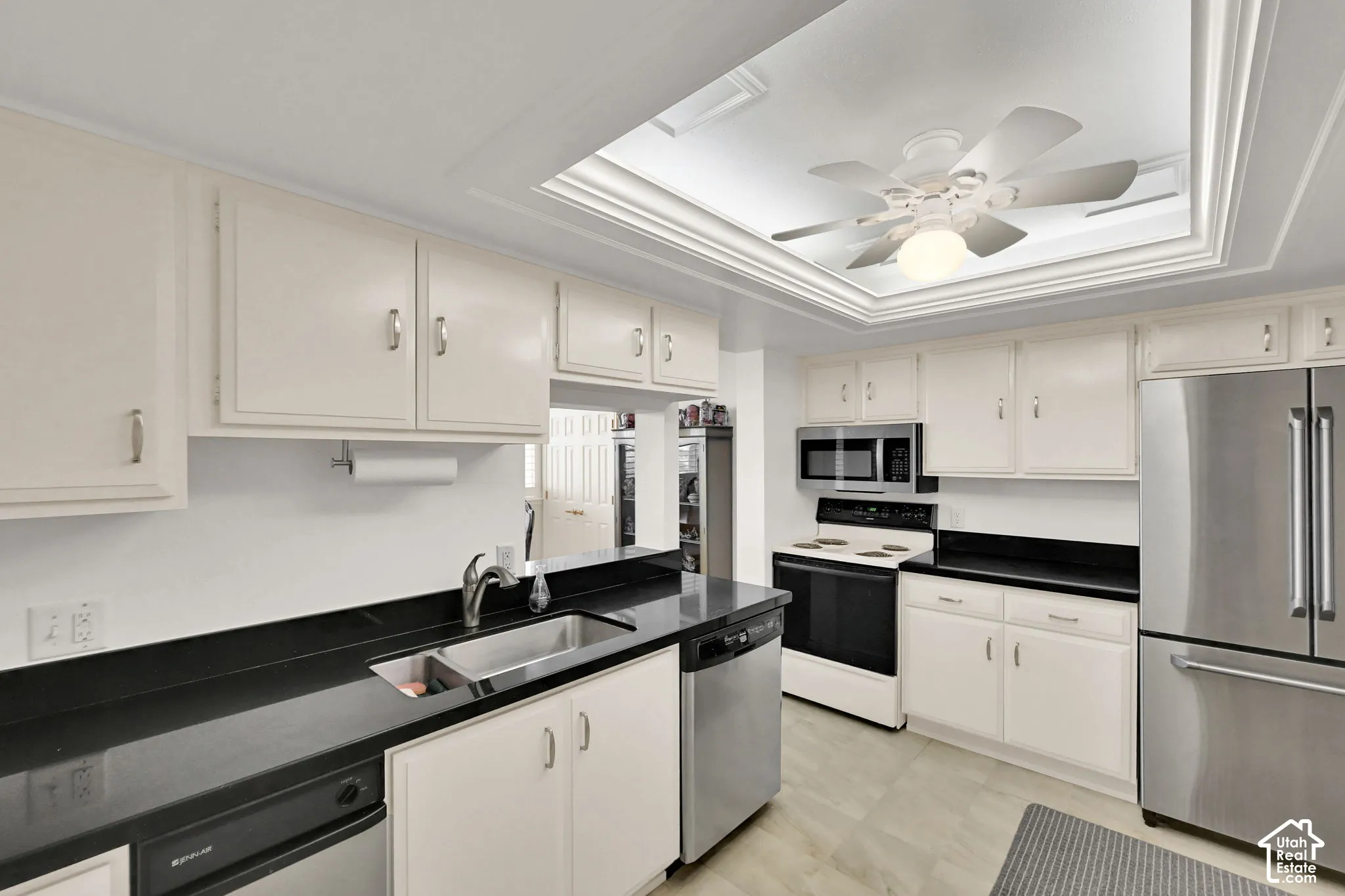 White cabinetry with silver-tone hardware, black countertops, undermount sink, and stainless steel appliances