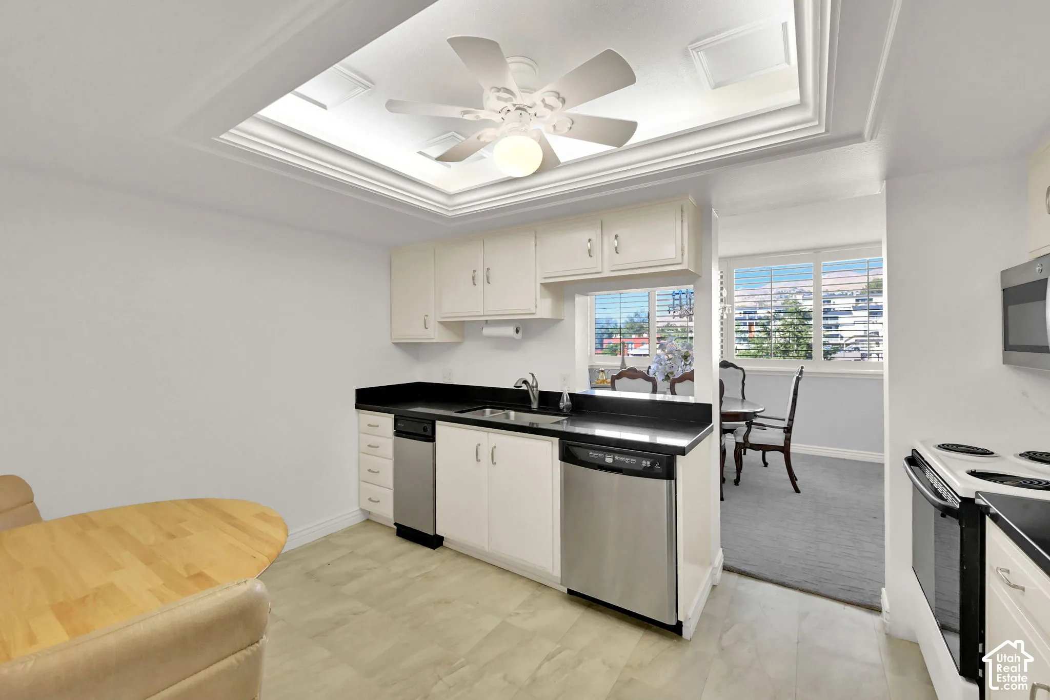 Kitchen featuring a tray ceiling with a ceiling fan, light-toned cabinetry, stainless steel appliances, dark countertops, and tile flooring