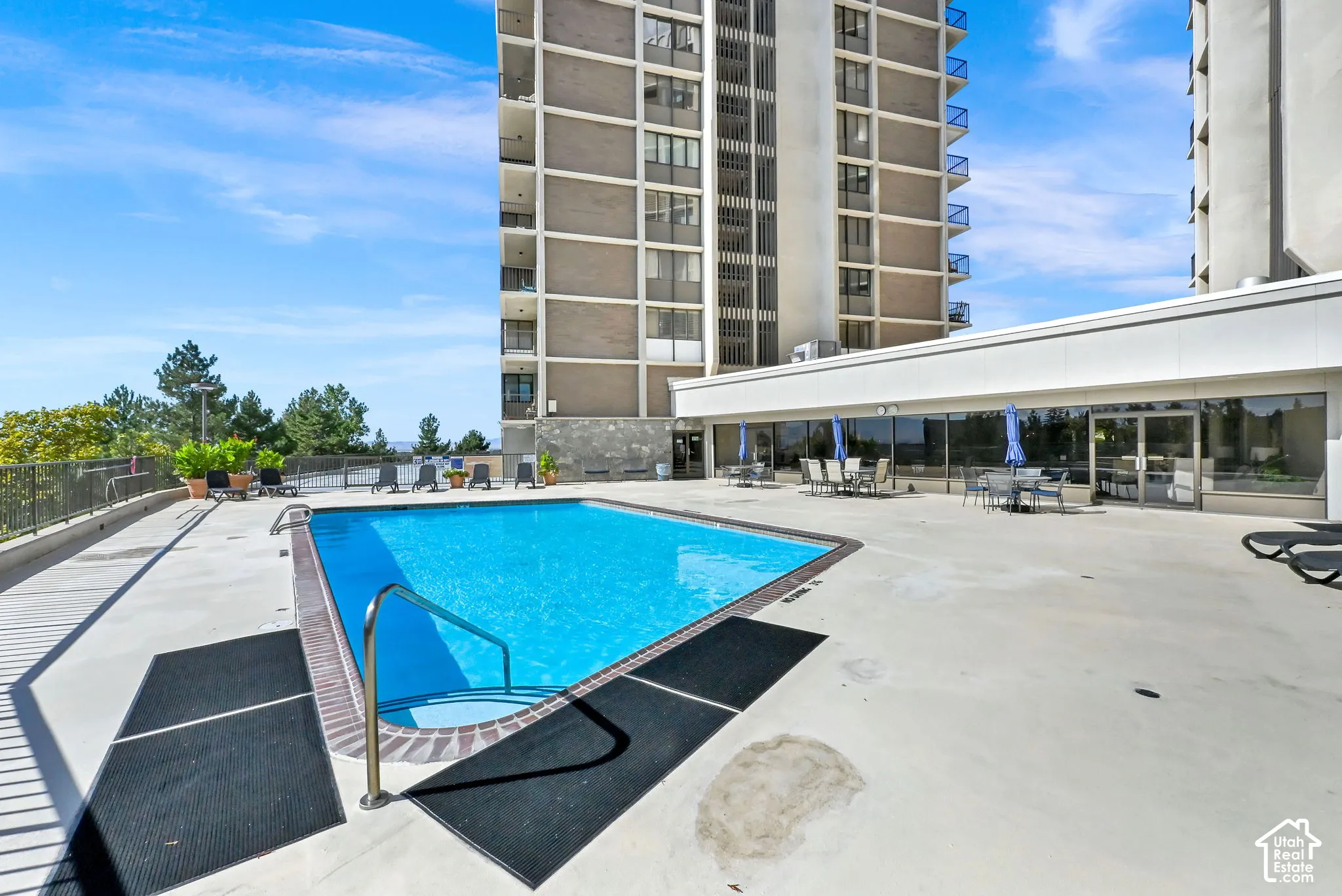 Outdoor swimming pool with integrated steps, surrounding paved patio, and a metal safety railing