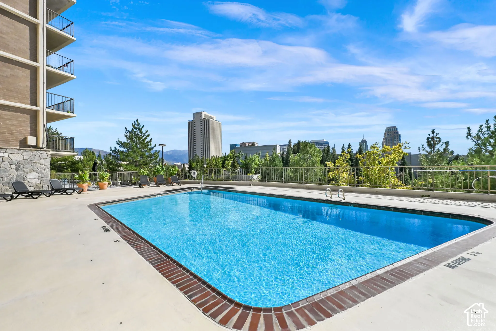 Outdoor swimming pool with a brick-lined perimeter, a concrete deck, and city buildings in the background