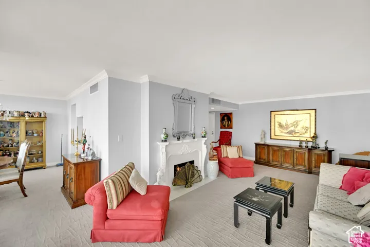 Open-concept living space featuring crown molding, a built-in fireplace with an ornate mantel, and carpeted flooring