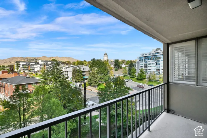 Outdoor balcony with a black metal railing and concrete flooring, offering expansive city and mountain scenery