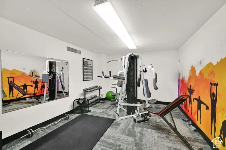 Dedicated fitness room featuring professional-grade exercise equipment, dark rubber flooring, bright overhead LED lighting, and motivational wall graphics