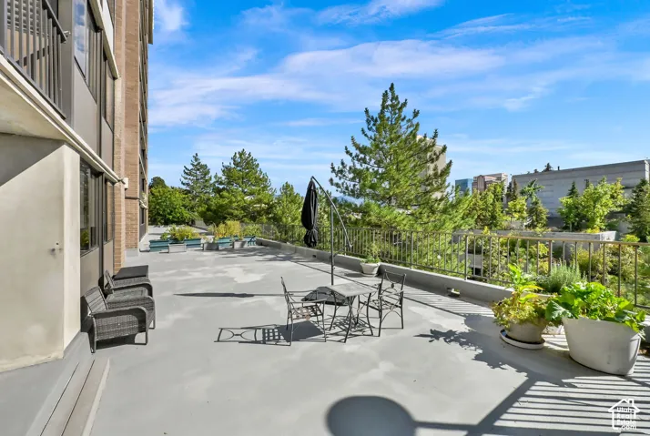 Expansive outdoor terrace featuring a concrete surface, metal railing, and surrounding greenery