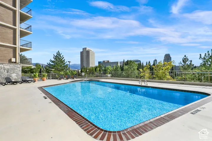 Outdoor swimming pool with a brick-lined perimeter, a concrete deck, and city buildings in the background