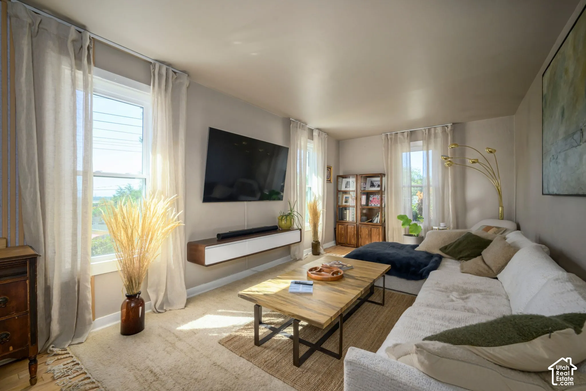 Wall-mounted television with floating media console, multiple windows with natural light, wood-finish flooring, and light-toned walls