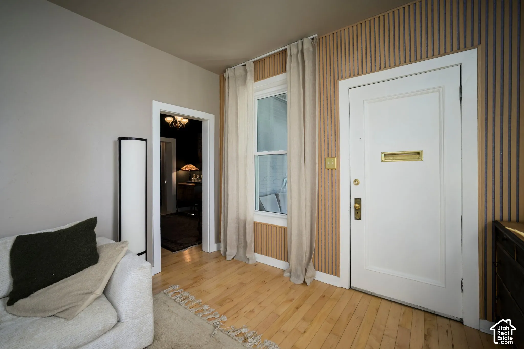 Hardwood flooring, painted interior door with brass hardware, window with trim, patterned wall covering, neutral wall paint