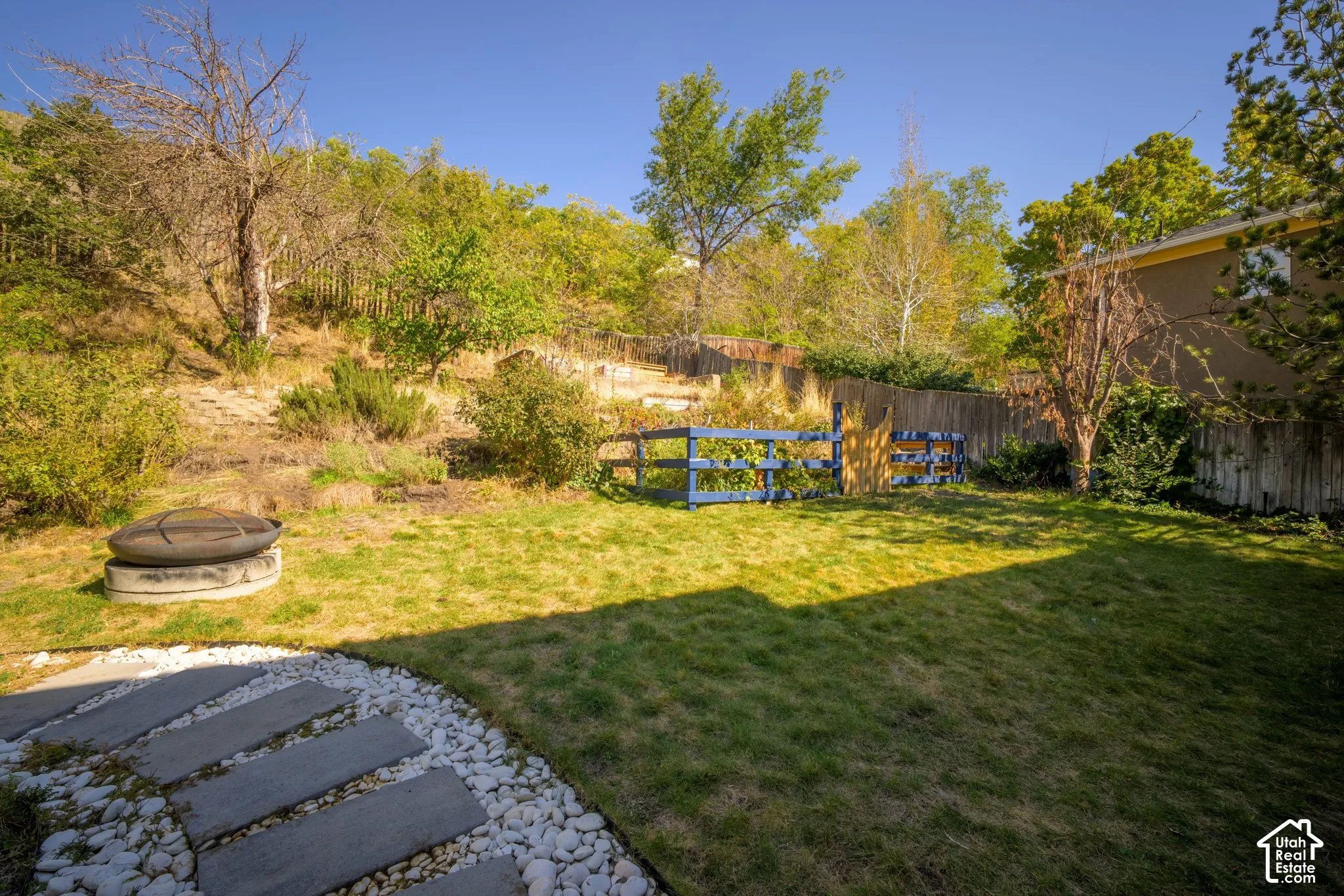 Expansive backyard featuring a manicured lawn, established landscaping, a privacy fence, and a stone fire pit