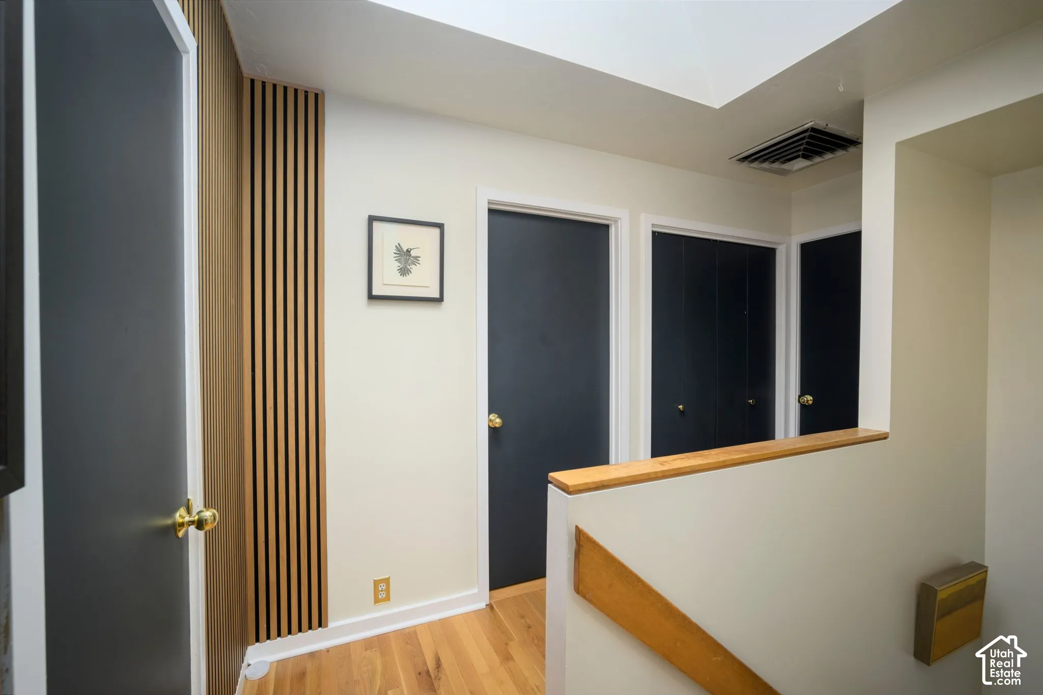 Wood-finish slat wall accent, light wood flooring, skylight, white walls, and dark-paneled doors