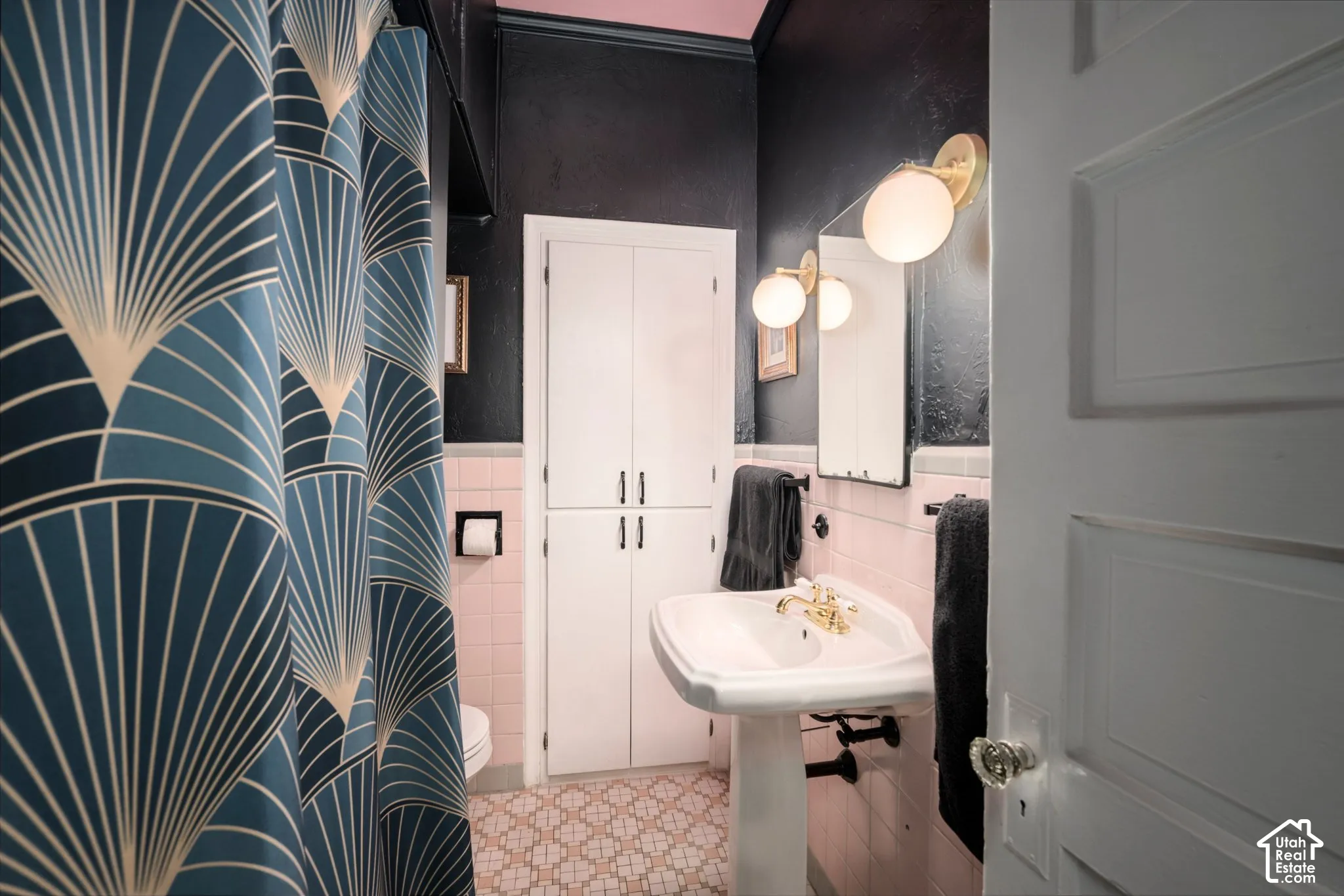 Pedestal sink with brass-finish faucet, wall-mounted spherical light fixtures, and white built-in cabinetry