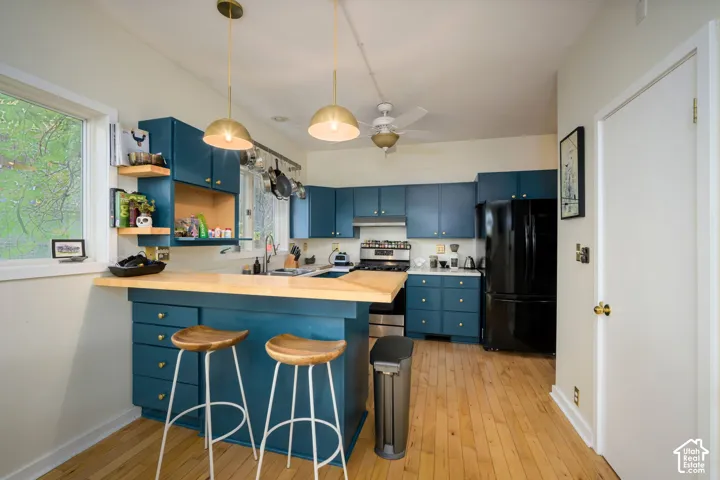 Kitchen featuring custom teal cabinetry, light wood-finish countertops, stainless steel range, and wood-finish flooring