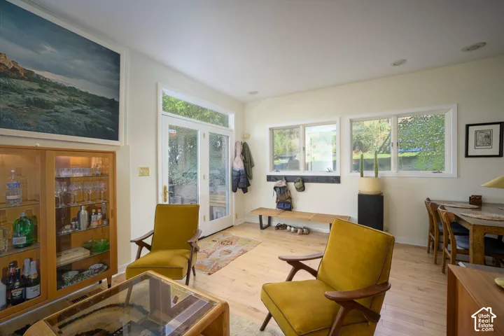 Light wood-finish flooring throughout, double glass-paneled doors with transom, multiple windows providing ample ambient light, recessed ceiling lighting, and a built-in display cabinet