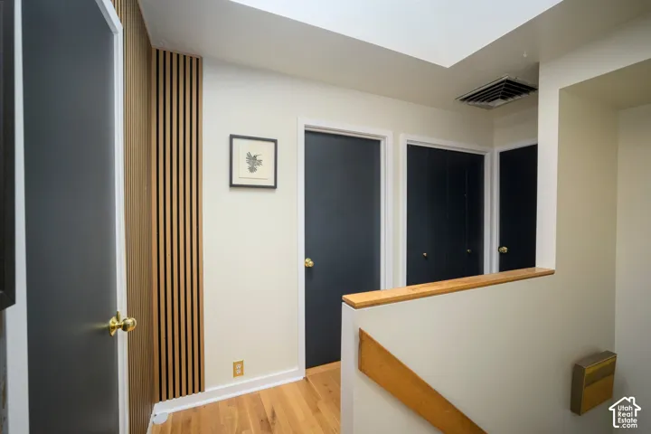 Wood-finish slat wall accent, light wood flooring, skylight, white walls, and dark-paneled doors