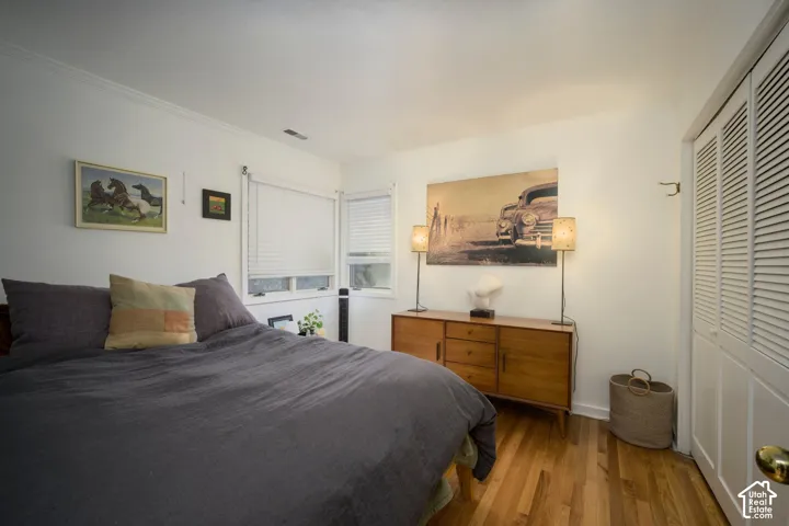 Hardwood flooring, white walls, crown molding, double windows with blinds, and a built-in louvered closet