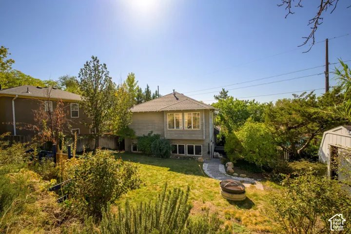 Expansive sloped yard featuring a manicured lawn, established shrubs, a stone pathway, and a fire pit area