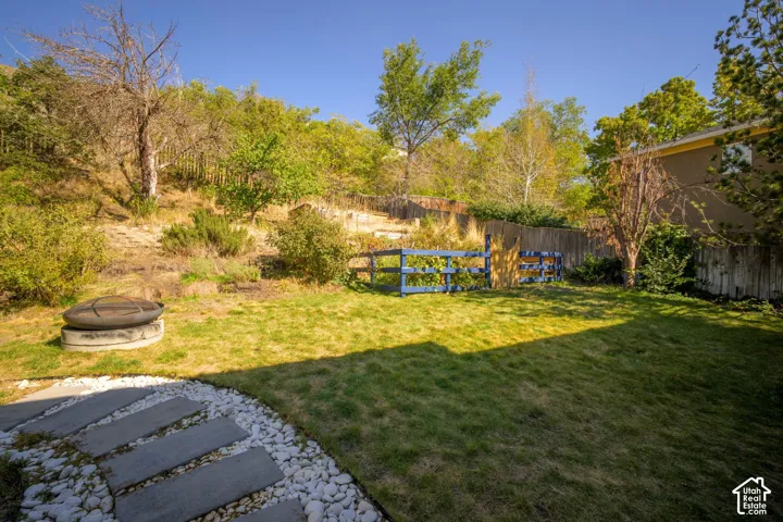 Expansive backyard featuring a manicured lawn, established landscaping, a privacy fence, and a stone fire pit