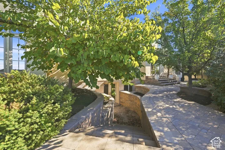 Stone paver pathway leading to entry with multiple steps, flanked by retaining walls and mature trees
