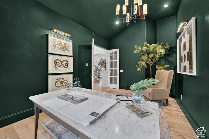 Room featuring dark green painted walls, hardwood flooring, a marble-top desk, and a multi-arm chandelier