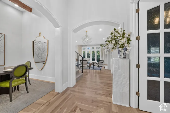 Herringbone wood-finish flooring, arched doorways, a white French door with glass panels, a dark wood ceiling beam, and a wrought iron staircase railing